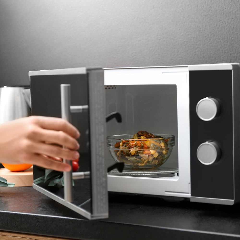 Young woman using microwave oven on table in kitchen
