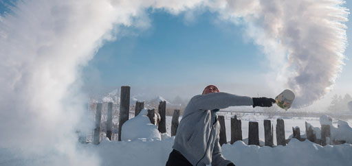 the man from the ladle pours the boiling water up into the sky in an arc in freezing weather